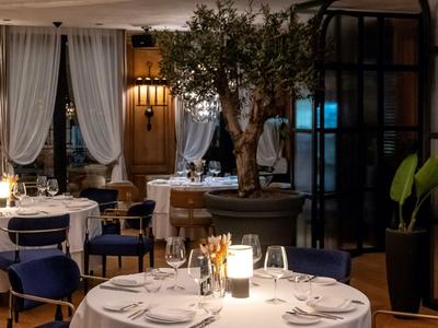 Elegancka restauracja z nakrytymi stołami, niebieskimi krzesłami i miękkim oświetleniem.