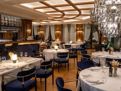 Elegancka restauracja z okrągłymi nakrytymi stołami, niebieskimi krzesłami i stylowym oświetleniem.