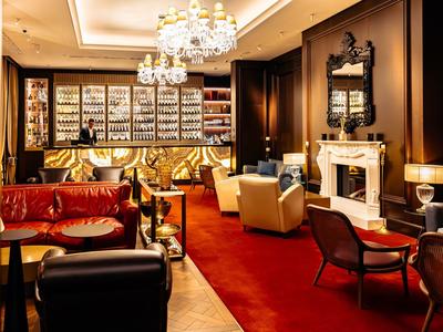 Elegancki bar hotelowy z złotymi żyrandolami, czerwonym dywanem i wygodnymi fotelami.