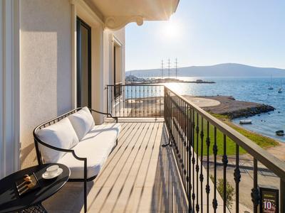Balkon mit weißem Sofa und Tisch, Blick auf Meer und Küste bei sonnigem Himmel.