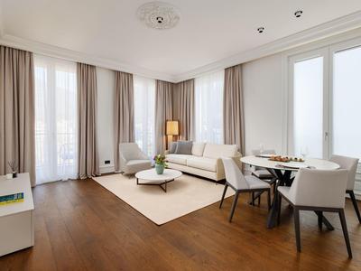 Helles Wohnzimmer mit Holzboden, weißen Möbeln, großen Fenstern und beigen Vorhängen.