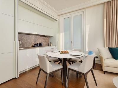 Kleiner Essbereich mit rundem Tisch, vier Stühlen, moderner Küche und Sofa in hellem Raum.