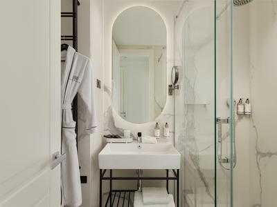 Kleines, modernes Badezimmer mit weißem Waschbecken, ovalem Spiegel und Glastür-Dusche mit Marmorwand.