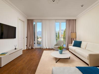 Helles Wohnzimmer mit weißem Sofa, Teppich, Couchtisch, TV an der Wand und Holzfußboden.