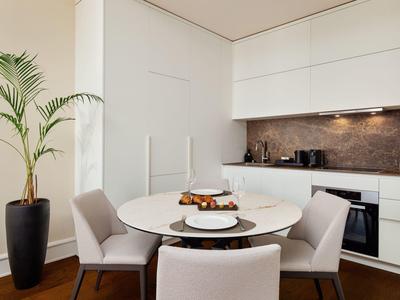 Moderner Essbereich mit runder weißer Tischplatte, vier grauen Stühlen und Topfpflanze in hellem Raum.