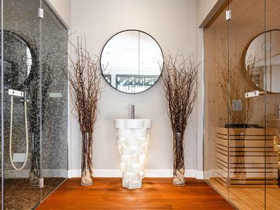 Moderner Badezimmerbereich mit Glasdusche, rundem Spiegel, weißem Waschtisch und Holzboden.