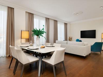 Heller Wohn- und Essbereich mit Holzboden, weißen Möbeln und großen Fenstern mit Vorhängen.