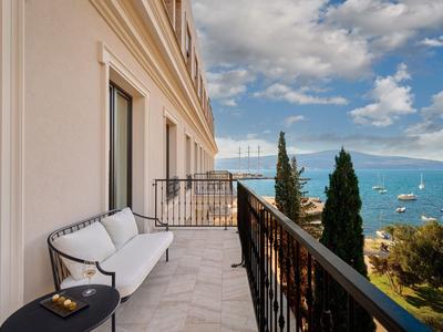 Balkon mit weißem Sofa und schwarzem Beistelltisch, Blick auf Meer, Boote und bewölkten Himmel.