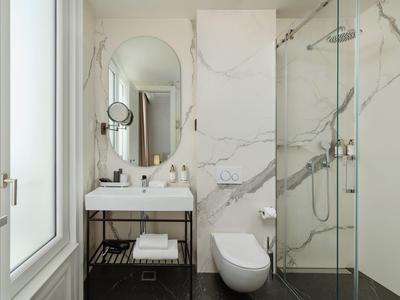 Helles Badezimmer mit Marmorwänden, Glasdusche, Wand-WC und Waschbecken mit großem Spiegel.