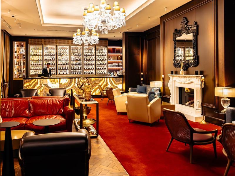 Elegantes Wohnzimmer mit rotem Teppich, Ledersesseln, Kronleuchtern und Kamin im warmen Licht.