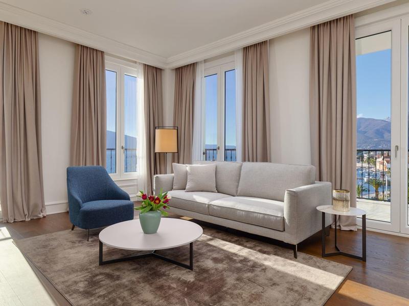 Helles Wohnzimmer mit großem Fenster, grauem Sofa, blauem Sessel und rundem weißen Tisch.