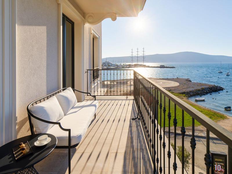 Balkon mit weißem Sofa und Tisch, Blick auf Meer und Küste bei sonnigem Himmel.