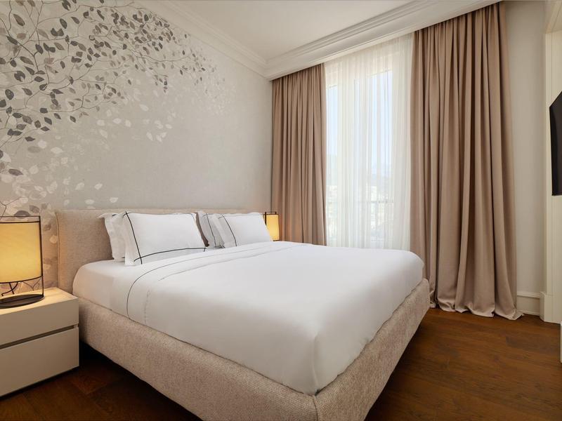 Helles Schlafzimmer mit großem Bett, weißen Wänden, Vorhängen und hellem Holzfußboden.