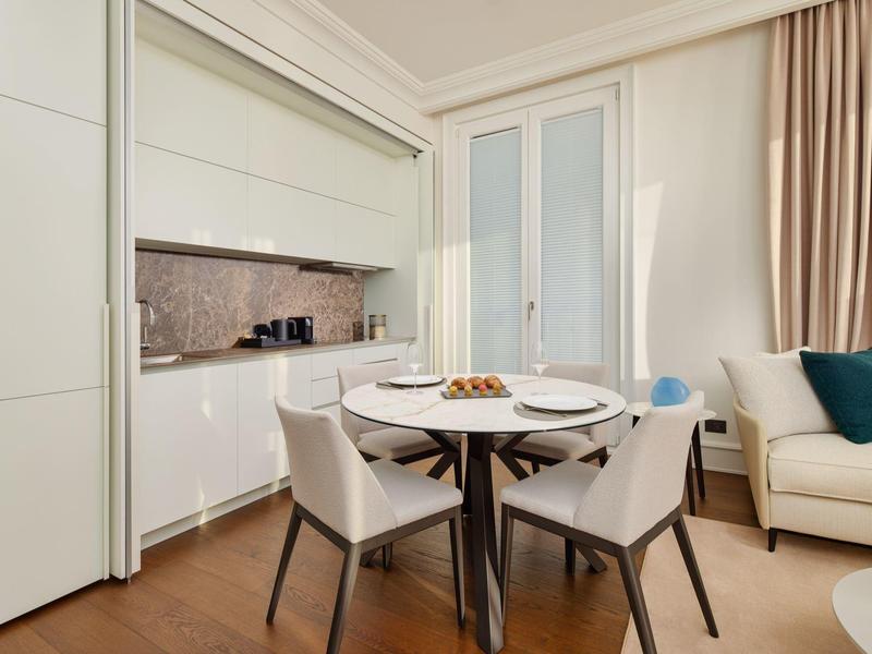 Kleiner Essbereich mit rundem Tisch, vier Stühlen, moderner Küche und Sofa in hellem Raum.