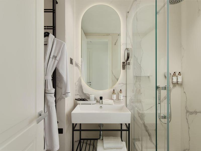 Kleines, modernes Badezimmer mit weißem Waschbecken, ovalem Spiegel und Glastür-Dusche mit Marmorwand.