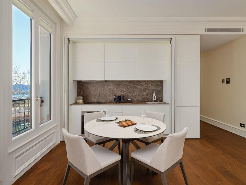 Moderner Essbereich mit rundem Tisch, vier weißen Stühlen, offener Küche und großem Fenster mit Bergblick.