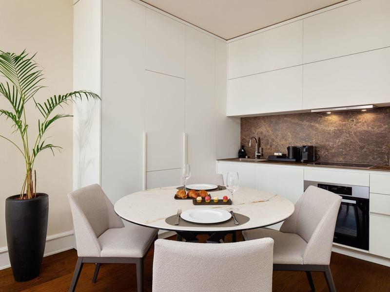 Moderner Essbereich mit runder weißer Tischplatte, vier grauen Stühlen und Topfpflanze in hellem Raum.