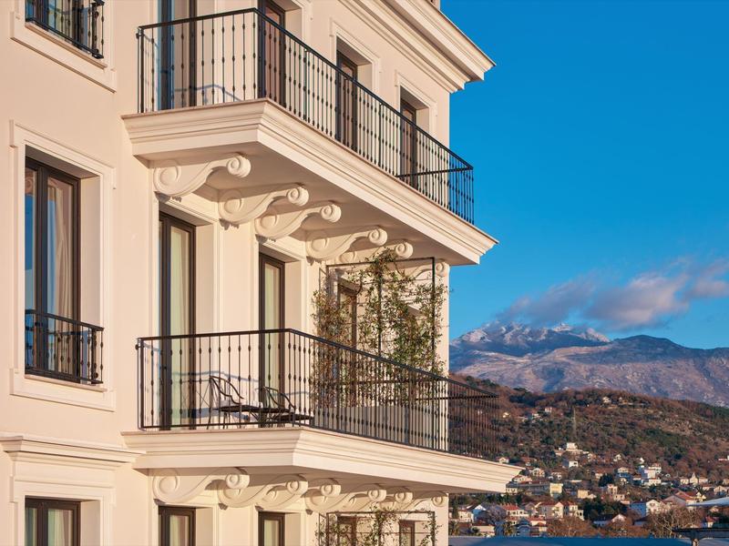 Ein heller Wohngebäudeeck mit Balkonen, im Hintergrund Berge unter blauem Himmel.
