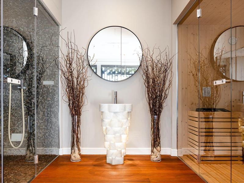 Moderner Badezimmerbereich mit Glasdusche, rundem Spiegel, weißem Waschtisch und Holzboden.