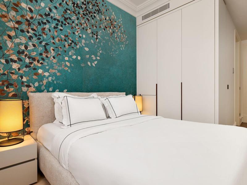 Schlafzimmer mit großem weißen Bett, Nachttischen mit Lampen und Blumentapete in Blau und Gold.