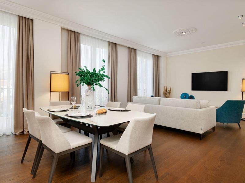 Heller Wohn- und Essbereich mit Holzboden, weißen Möbeln und großen Fenstern mit Vorhängen.