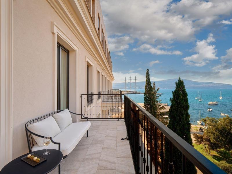 Balkon mit weißem Sofa und schwarzem Beistelltisch, Blick auf Meer, Boote und bewölkten Himmel.
