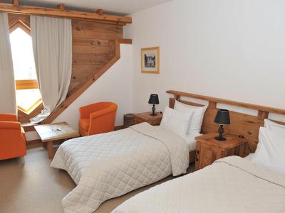 Hotelkamer met twee eenpersoonsbedden, houten meubels en oranje fauteuils bij het raam.