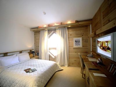 Gezellige hotelkamer met houten muren, tweepersoonsbed, bureau en televisie.