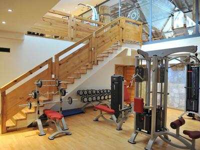 Fitnessraum mit Kraftgeräten, Hanteln und einer Holztreppe im Hintergrund