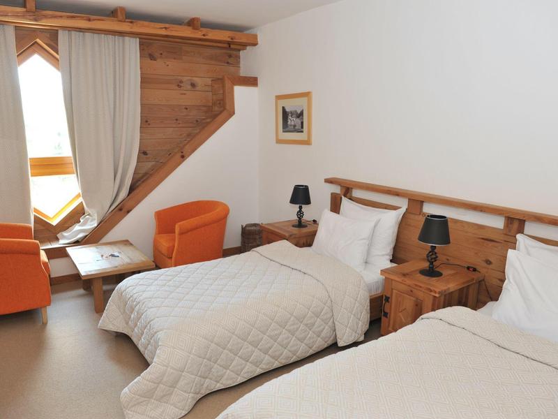 Hotelkamer met twee eenpersoonsbedden, houten meubels en oranje fauteuils bij het raam.