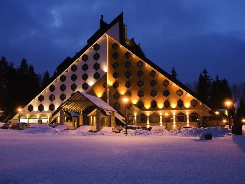 Verlicht driehoekig hotelgebouw in besneeuwd winterlandschap in de nacht.