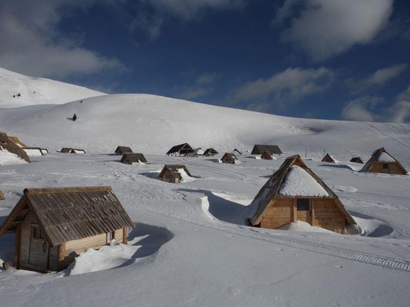 Met sneeuw bedekte houten huisjes in een bergdorp in de winter onder een blauwe lucht.