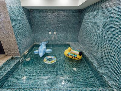 Innen-Pool mit türkisfarbenen Mosaikfliesen und bunten aufblasbaren Spielzeugen im Wasser.