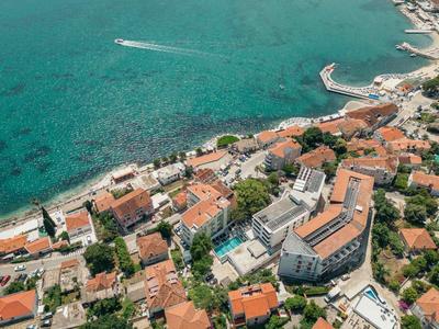 Luftaufnahme einer Küstenstadt mit roten Dächern, blauem Meer und einer kleinen Hafenanlage.