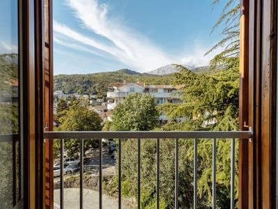 Vista da un balcone con ringhiera su alberi verdi e case sotto un cielo azzurro.
