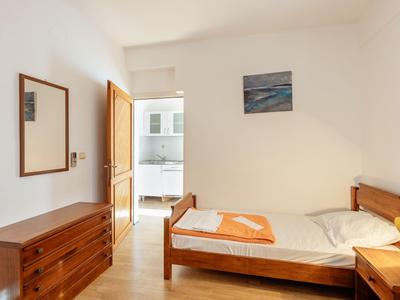 Einfaches helles Schlafzimmer mit Holzbetten, Kommode, Spiegel und einem Bild an der Wand.