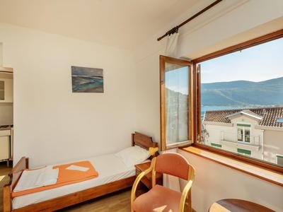 Kleines Zimmer mit Einzelbett, großem Fenster und Blick auf Berge und Häuserdach.