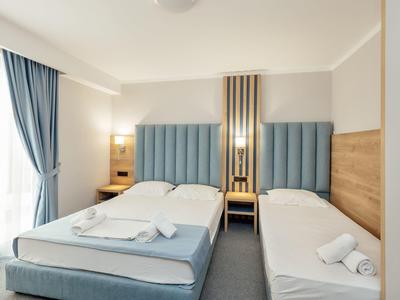 Schlichtes Hotelzimmer mit zwei Betten, blauen gepolsterten Kopfstützen und hellen Wänden.