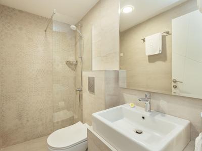 Helles Badezimmer mit weißem Waschbecken, Toilette, Duschbereich und großem Spiegel an der Wand.