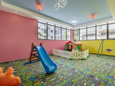 Bunter Indoor-Spielbereich mit Rutsche, Schaukel, Spielhaus und Teppich mit Städte-Design.