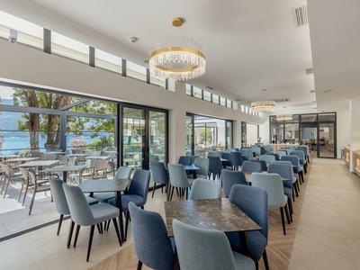 Moderner Speisesaal mit blauen Stühlen, großen Fenstern und heller Beleuchtung, offene Terrasse sichtbar.