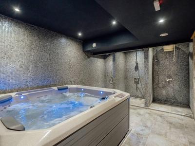 Moderner Wellnessraum mit beleuchtetem Whirlpool, Mosaik-Wänden und Duschbereich in dunklem Design.