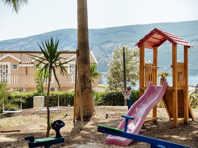 Kleiner Spielplatz mit Rutsche, Schaukel und Bäumen vor Berglandschaft und Häusern.