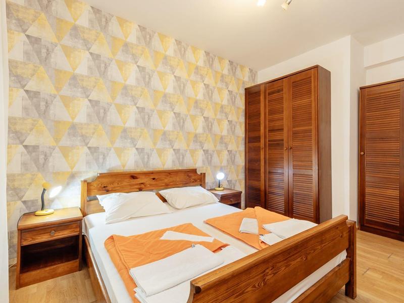 Helles Schlafzimmer mit Holzmöbeln, gemusteter Wand und zwei orangefarbenen Handtüchern auf dem Bett.