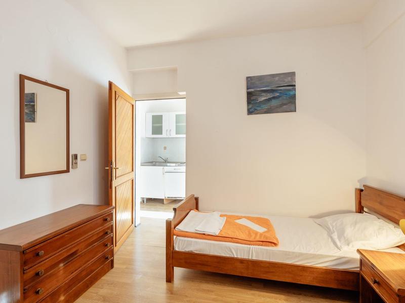 Einfaches helles Schlafzimmer mit Holzbetten, Kommode, Spiegel und einem Bild an der Wand.