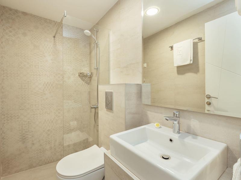 Helles Badezimmer mit weißem Waschbecken, Toilette, Duschbereich und großem Spiegel an der Wand.