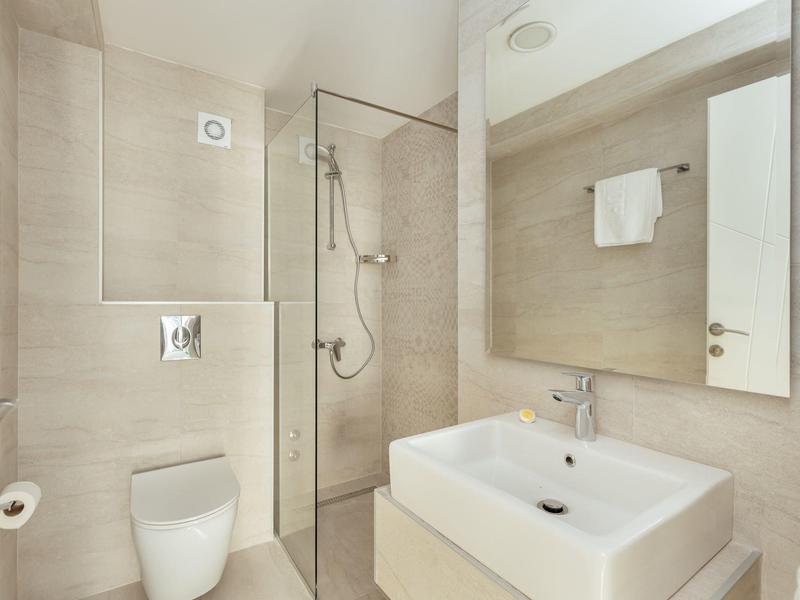 Modernes, helles Badezimmer mit Glastrennwand, braunen Fliesen, weißem Waschbecken und WC.