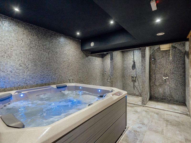 Moderner Wellnessraum mit beleuchtetem Whirlpool, Mosaik-Wänden und Duschbereich in dunklem Design.
