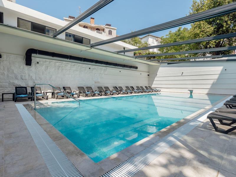 Moderner Außenpool mit klar blauem Wasser, Sonnenliegen und Pergola unter blauem Himmel.