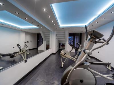 Moderner Fitnessraum mit Trainingsgeräten, großem Spiegel und indirekter Beleuchtung.